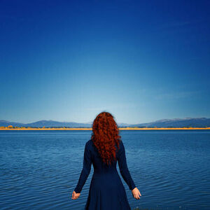 Umělecká fotografie Redhead in blue dress faces rippled lake, Anna Gorin, (40 x 40 cm)